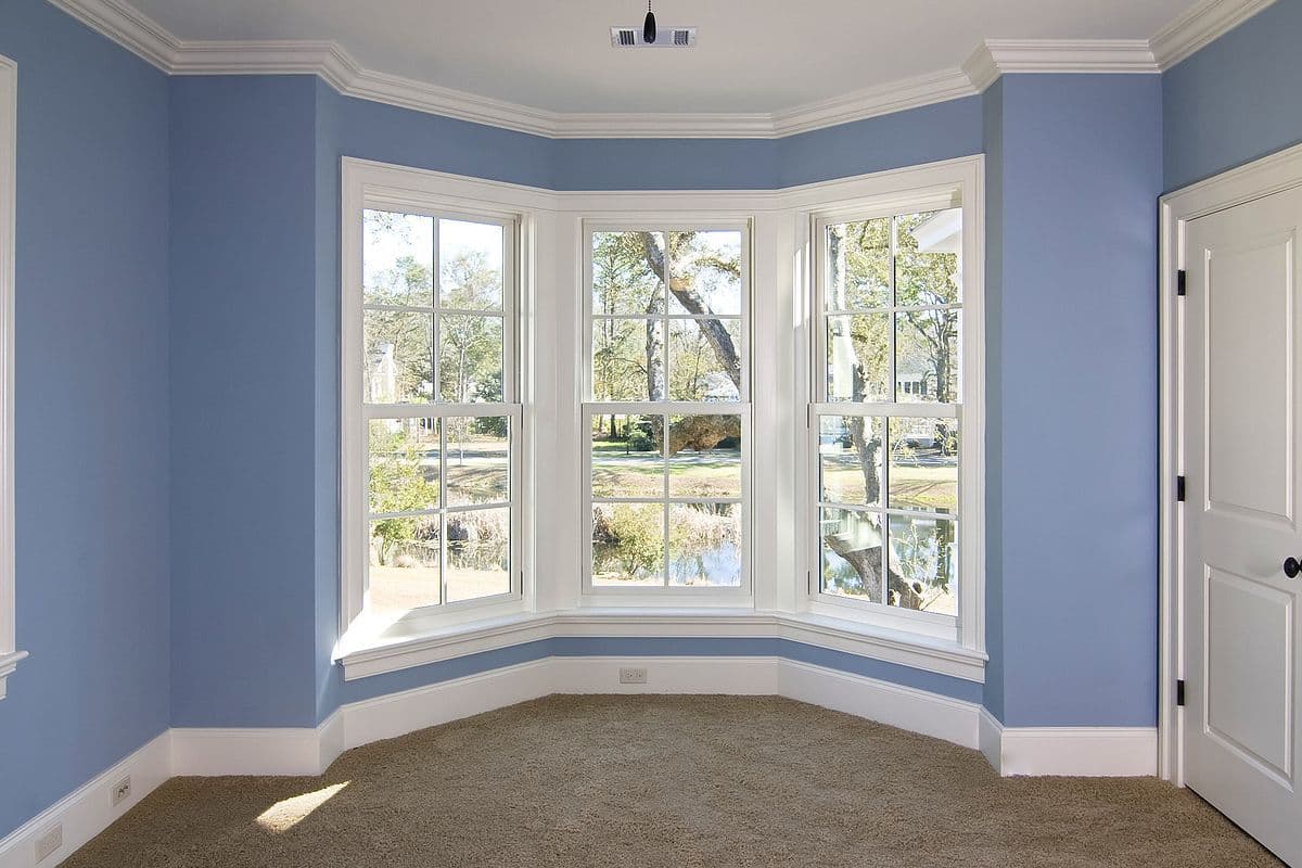 A blue bedroom with double-hung windows looking out onto a yard with a pond.