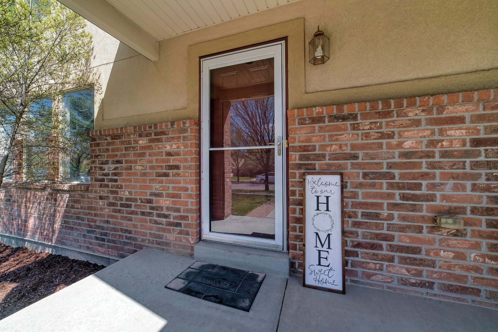 A tan and brick house with a brown entry door and white glass storm door.