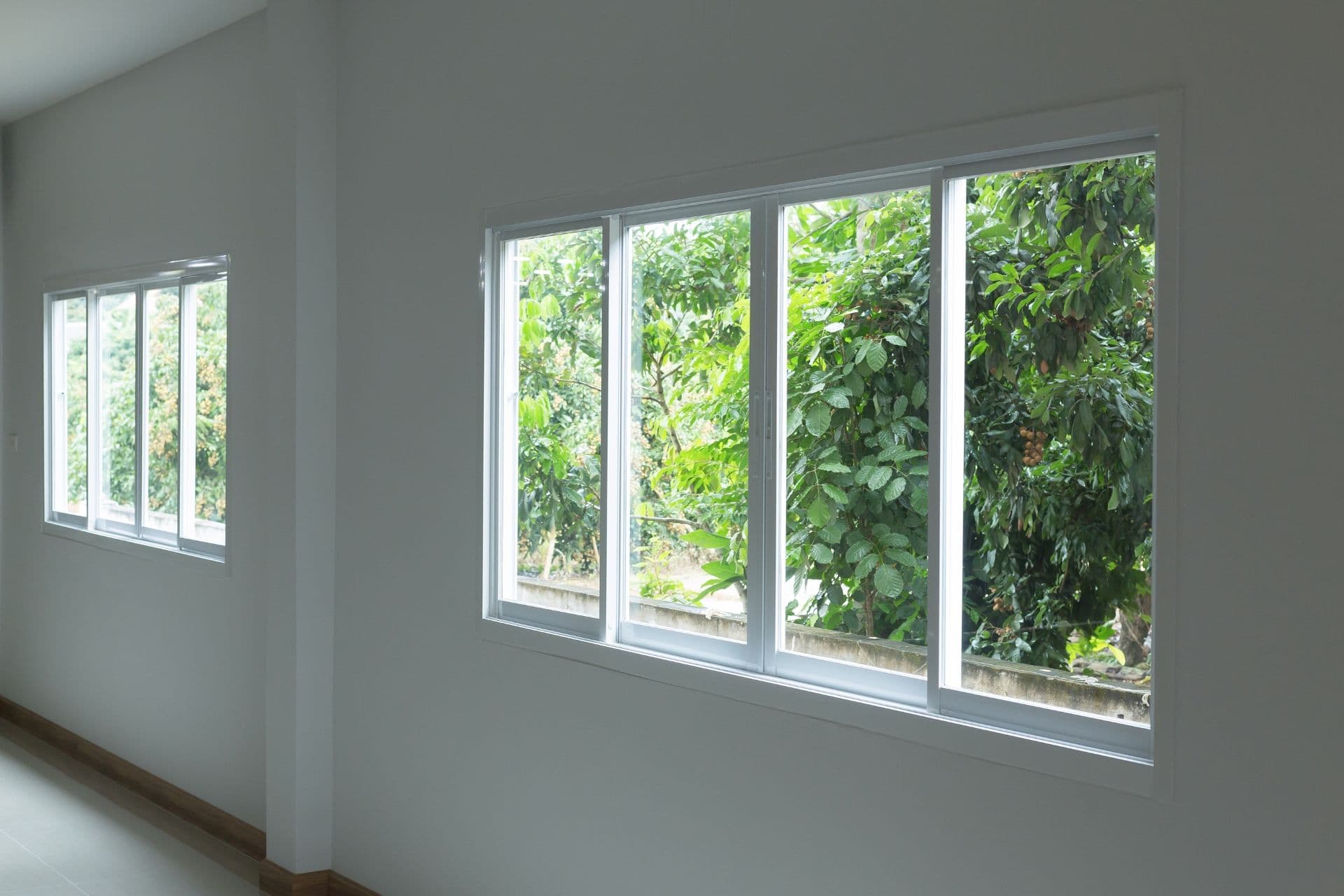 Sliding windows in a white room overlook a yard.