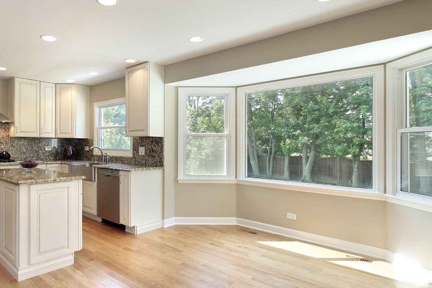 A beige kitchen with a large picture window overlooking a yard.