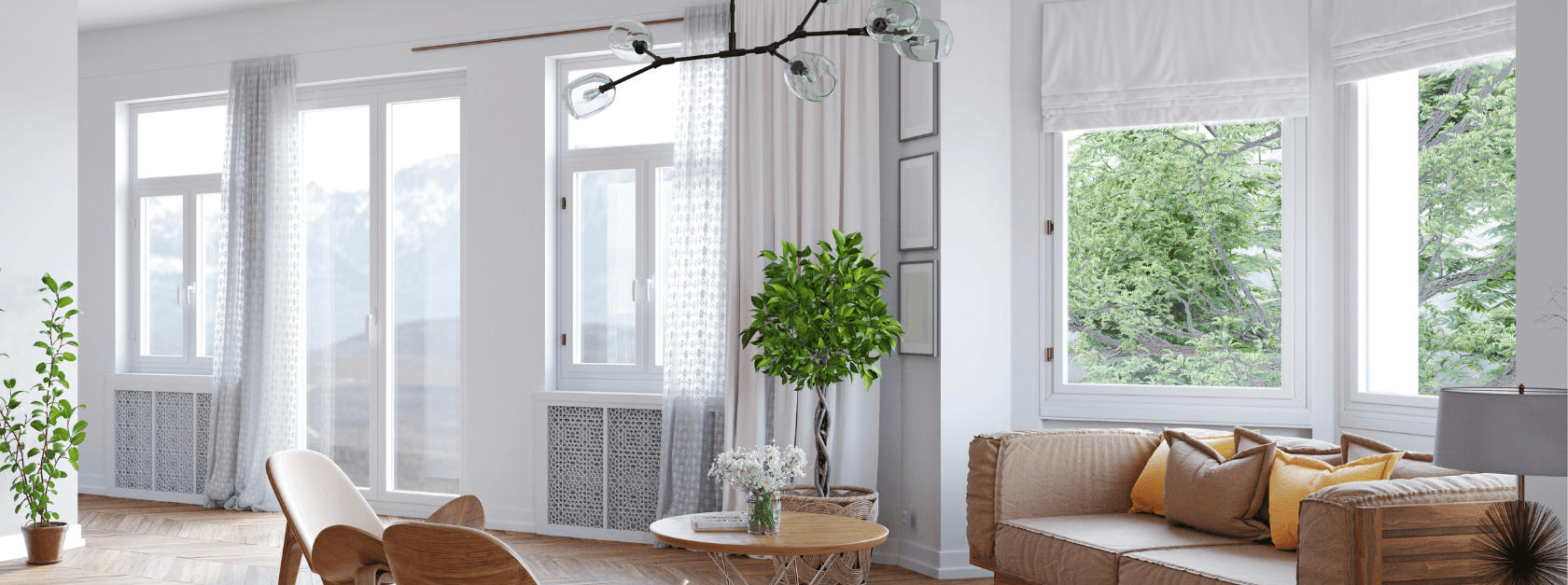 Bright, modern living room with large windows, white walls, and green views. Features a beige sofa, wooden chairs, plants, and a stylish chandelier.